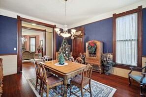 Une salle à manger avec une table en bois, des chaises, un lustre, un sapin de Noël et un grand miroir.