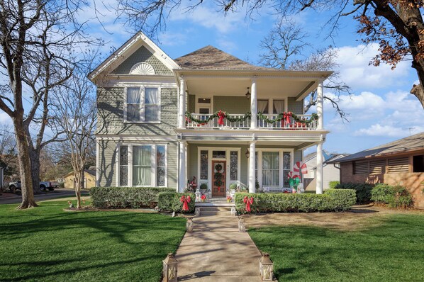 Une maison à deux étages avec un porche à l’avant, décoré de guirlandes et de décorations de Noël.