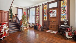 Un hall d’entrée spacieux avec un escalier en bois, un sapin de Noël et une grande fenêtre à vitraux.