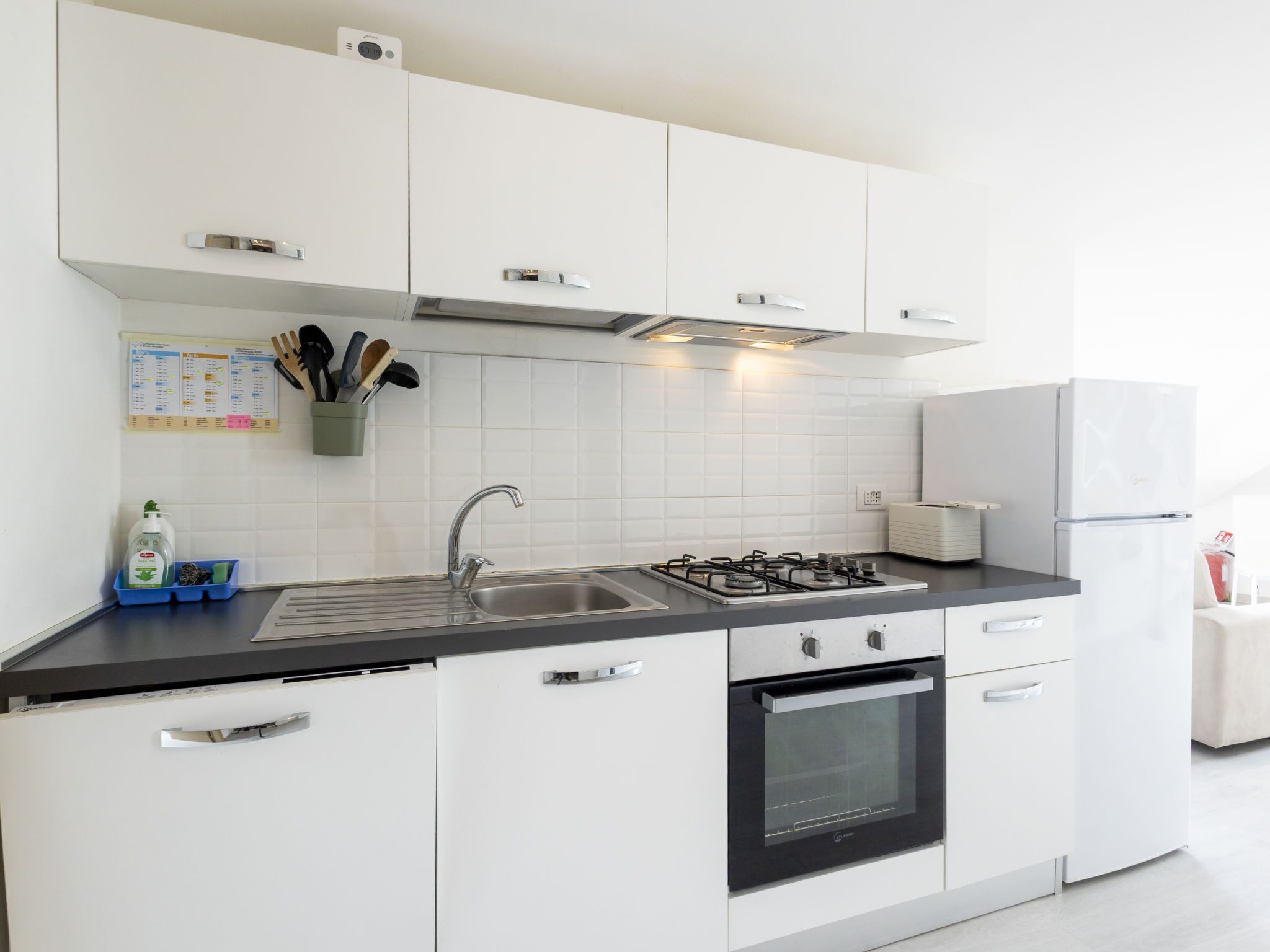 Una cocina moderna con armarios blancos, un lavamanos de acero inoxidable, una estufa a gas y un horno empotrado.