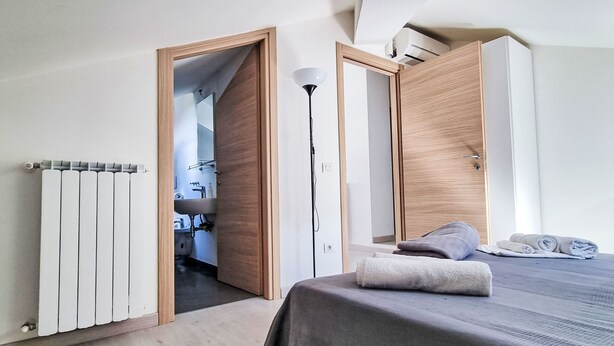 A bedroom with a bed, a radiator, a door leading to a bathroom, and a floor lamp. - Le Gemme by Interhome (Meina)