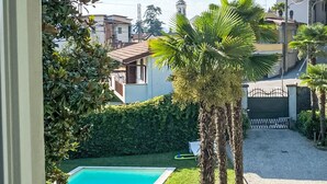 A swimming pool surrounded by palm trees and a hedge, with a view of houses in the background. - Le Gemme by Interhome (Meina)