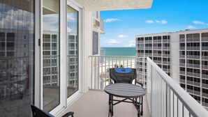 Ein Balkon mit Tisch und Stuhl, mit Blick auf einen Strand und ein Gebäude mit mehreren Balkonen.
