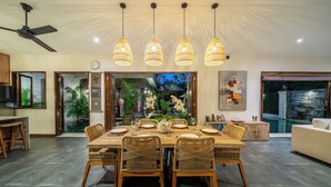 A modern dining area with a wooden table, wicker chairs, and pendant lights.