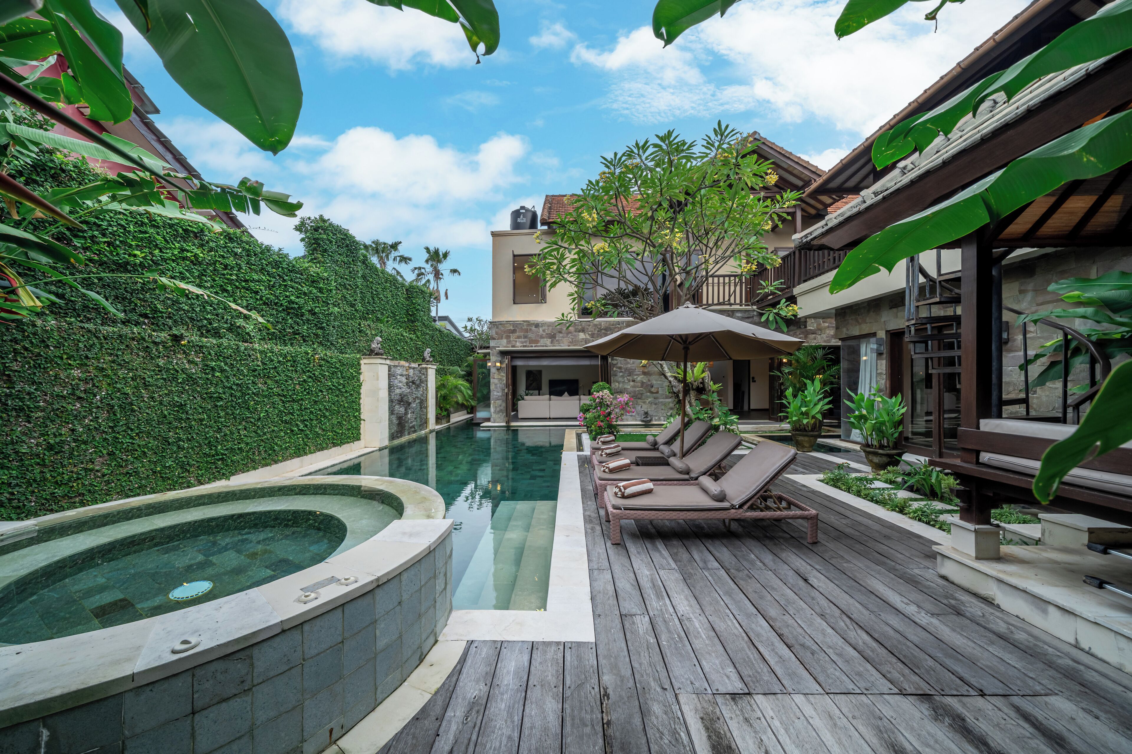 A pool area with a hot tub, lounge chairs, and a wooden deck.