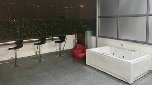 A modern bathroom with a large bathtub, a seating area with bar stools, and a view of a city skyline at night.