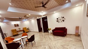 A spacious living area with a red sofa, two armchairs, and a coffee table. The room features a marble floor, ceiling fans, and recessed lighting.