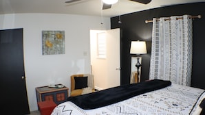 A bedroom with a bed, a chair, a nightstand, a lamp, and a door.