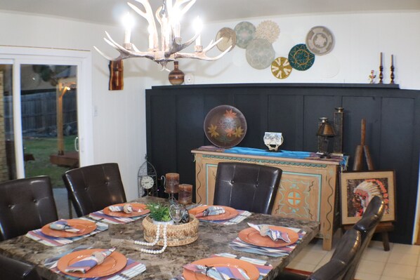 A dining area with a table set for six, surrounded by chairs. There is a chandelier above the table, and a decorative wall hanging above it. - Texas Dreamcatcher - Centrally Located (Longview)