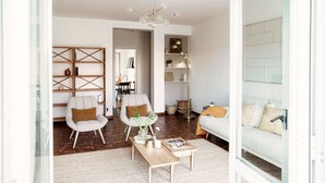 A modern living room with a sofa, two armchairs, a coffee table, a chandelier, and a bookshelf.