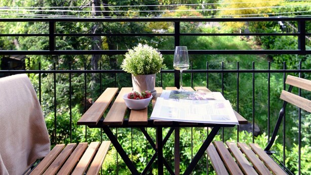 A wooden table with a potted plant, a glass of water, and a magazine on a balcony with a metal railing.