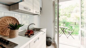 A modern kitchen with white cabinets, a stainless steel sink, and a view of a balcony with outdoor furniture.
