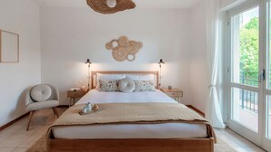 A bedroom with a bed, bedside tables, a chair, a hanging light fixture, and a window with curtains.