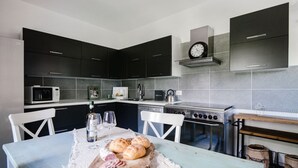 A modern kitchen with dark cabinets, a microwave, a stove, and a dining table set with bread and wine glasses. - Villa Solzago - MyHomeinComo (Tavernerio)