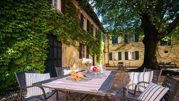 An outdoor patio with a table set for two, surrounded by metal chairs with striped cushions. - Villa Solzago - MyHomeinComo (Tavernerio)