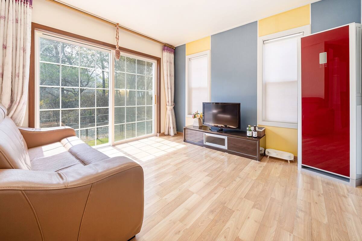 A modern living room with a leather sofa, a flat-screen TV, and a sliding glass door leading to a balcony.
