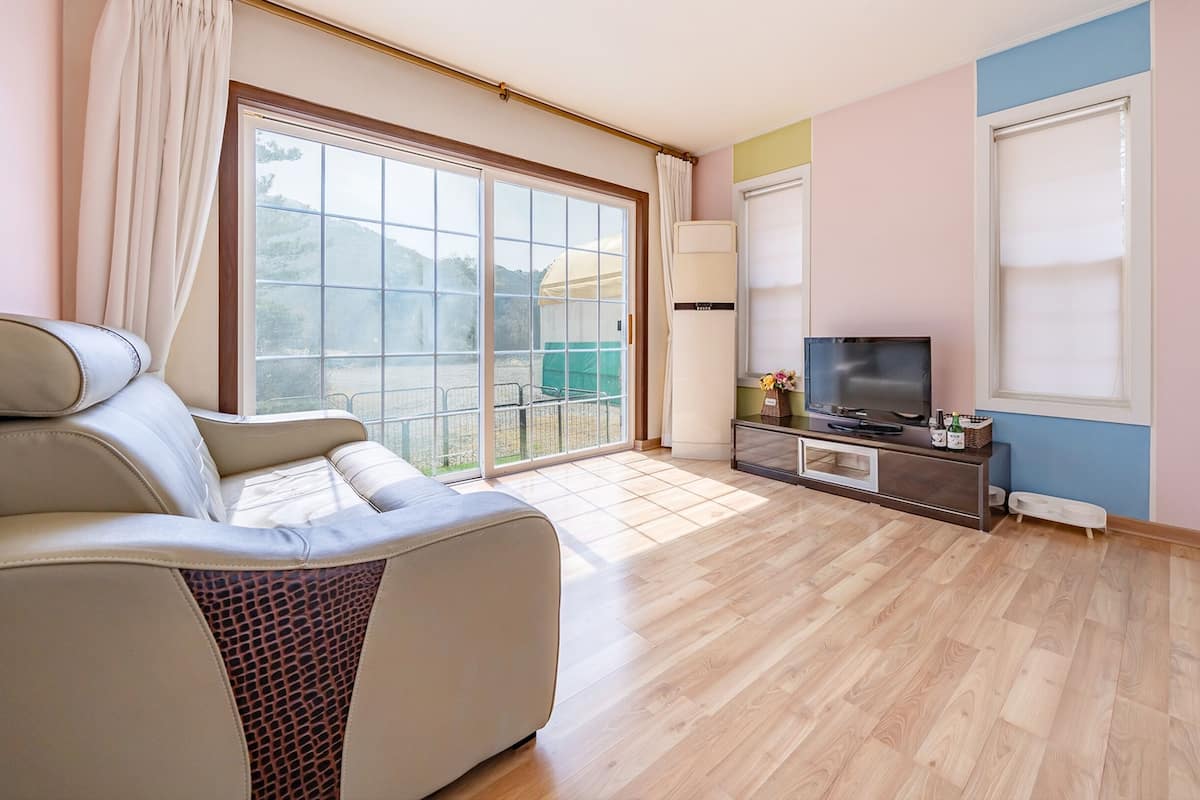 A modern living room with a sofa, a TV on a wooden cabinet, and large windows with curtains.