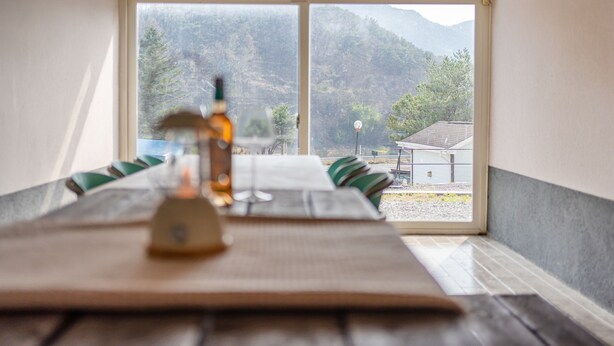 A dining table with a bottle and glasses, set against a window with a view of mountains and a building. - Yeongwol Nature & Retreat (Yeongwol)