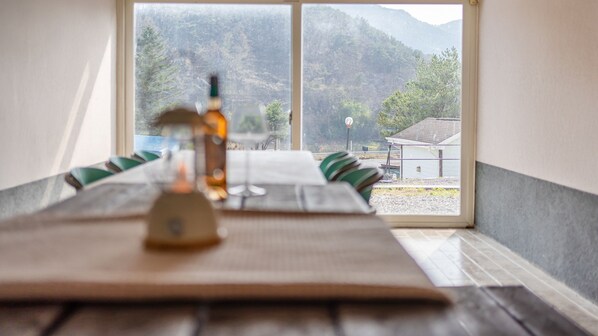 A dining table with a bottle and glasses, set against a window with a view of mountains and a building. - Yeongwol Nature & Retreat (Yeongwol)
