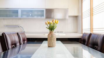 Un comedor moderno con una mesa de vidrio, un florero tejido con tulipanes amarillos y sillas de cuero.
