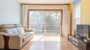 Una sala de estar con un sofá, una televisión y un ventanal corredero que da a un jardín.
