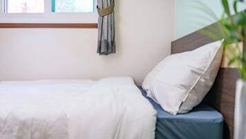 A neatly made bed with white bedding and a blue pillow, a wooden headboard, and a window with a curtain.