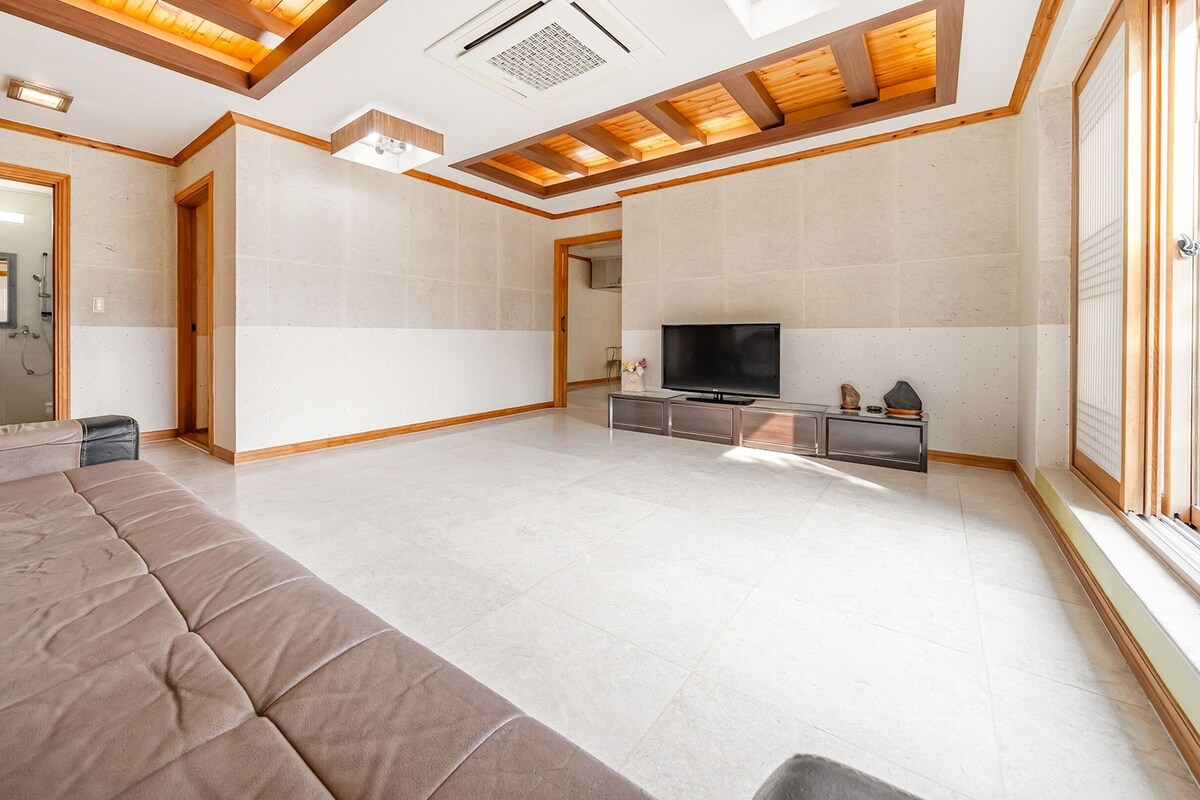A spacious living room with a large sofa, a flat-screen TV, and a stone fireplace.