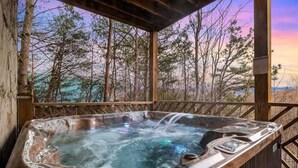 A hot tub with a wooden deck and a view of trees and mountains in the background.