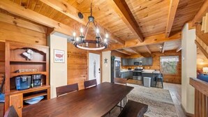A wooden cabin interior with a dining area, kitchen, and a chandelier.