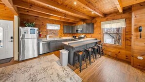 A log cabin kitchen with a central island, stainless steel appliances, and a large window.