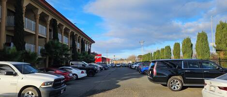 A parking lot with various cars, a building with columns and balconies, and a clear sky.