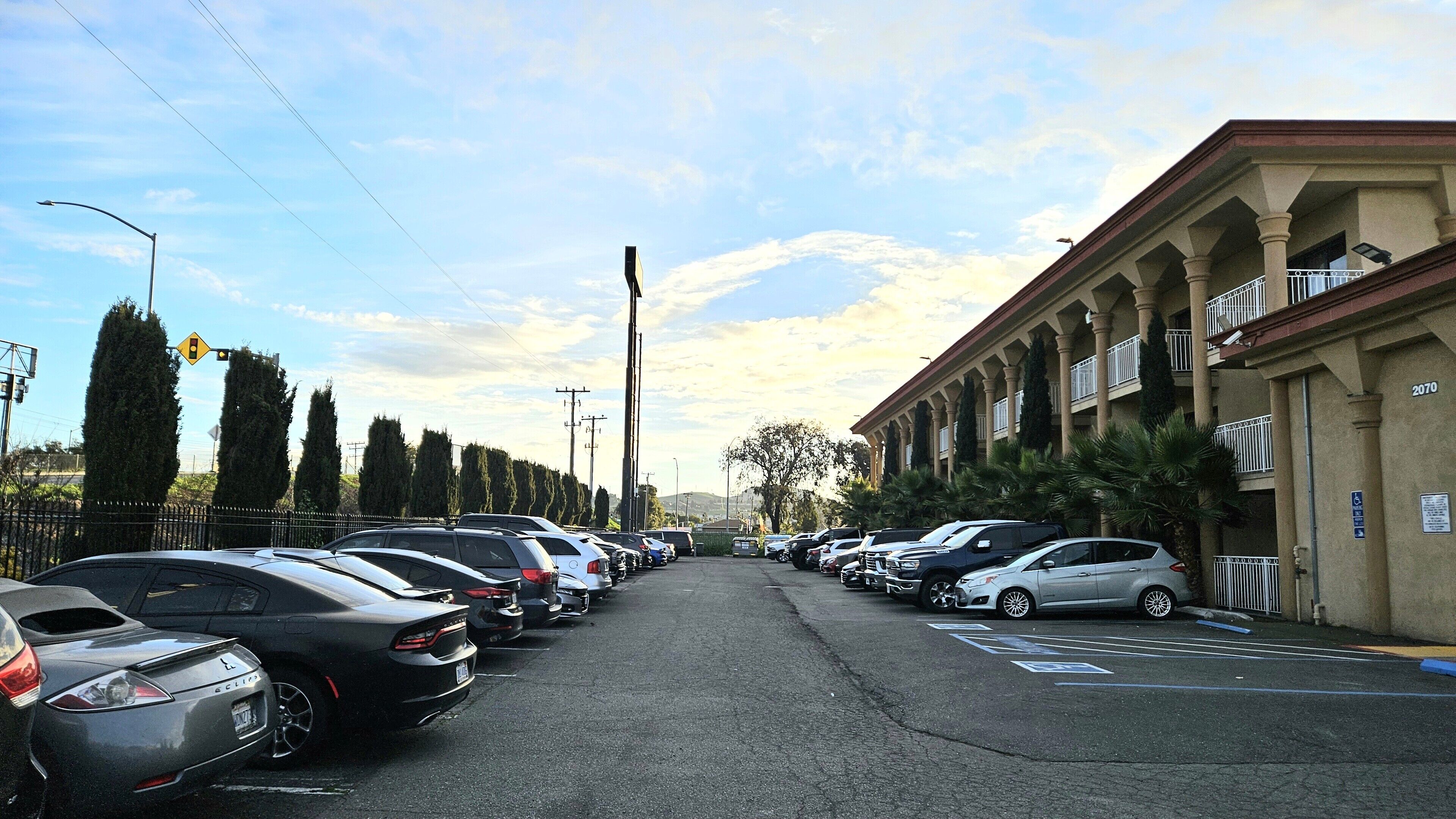 Un estacionamiento con varios autos, un edificio con columnas y balcones, y un cielo despejado.