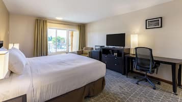 Habitación de hotel con cama, escritorio, silla, televisor y ventana con cortinas.