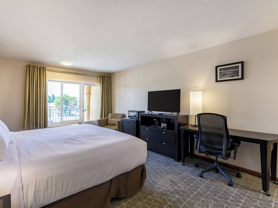 Habitación de hotel con cama, escritorio, silla, televisor y ventana con cortinas.