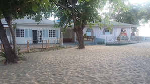 Un bâtiment situé en bord de mer, doté d’une terrasse en bois, d’un espace salon couvert et d’une cour entourée d’une clôture.