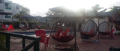 A poolside area with hanging egg chairs and red chairs.