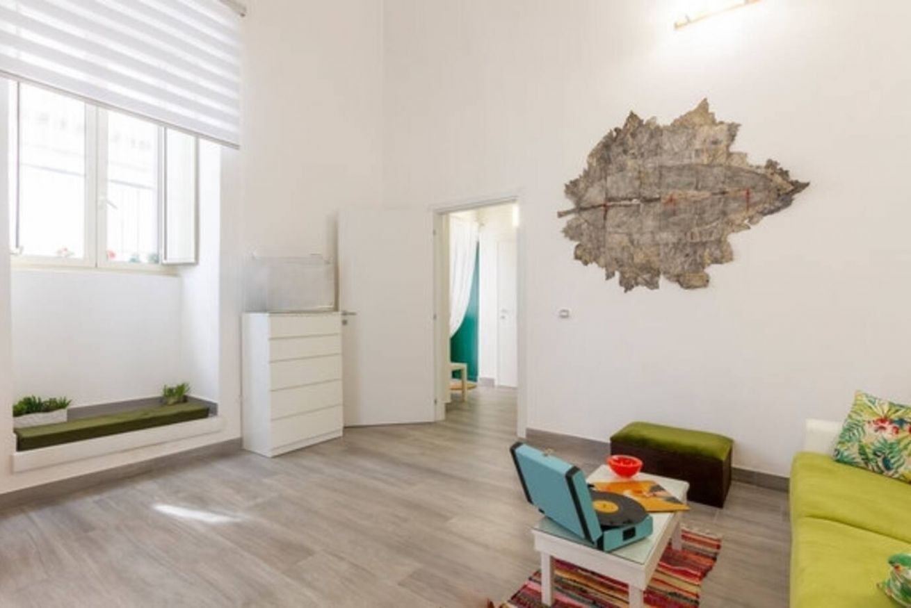A modern living room with a wooden floor, a green sofa, a coffee table with a record player, and a wall-mounted decorative piece.