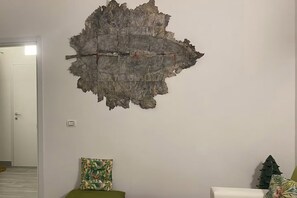 Una habitación con un gran elemento decorativo en la pared, un sofá verde y un pequeño árbol de Navidad.