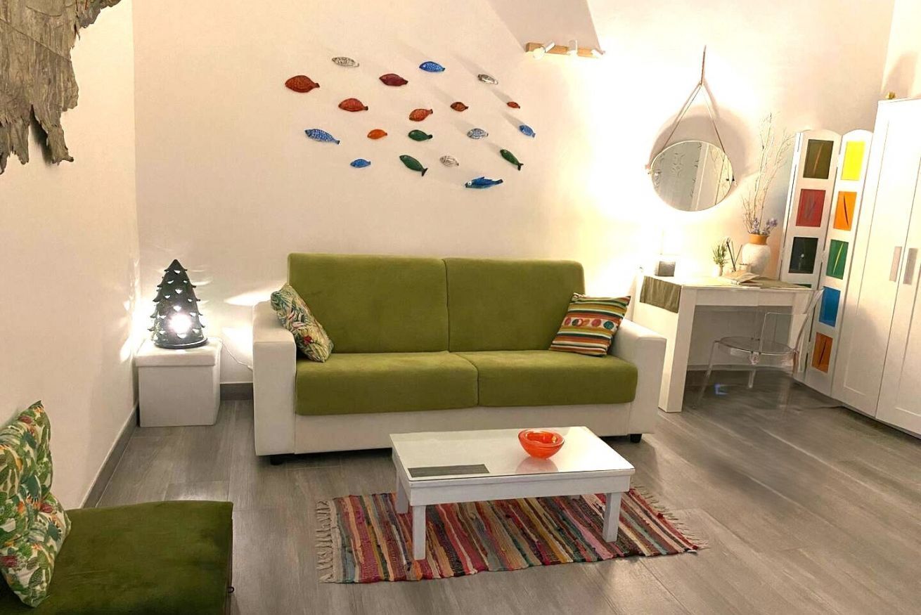 Un salon avec un canapé vert, une table basse blanche, un tapis coloré et un mur décoré d’ornements en forme de poisson.