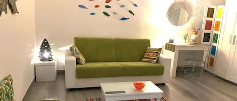 Ein Wohnzimmer mit einem grünen Sofa, einem weißen Couchtisch, einem bunten Teppich und einer Wand, die mit fischförmigen Dekorationen geschmückt ist.