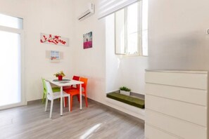 A modern, well-lit room with a dining table, chairs, and a small plant on a shelf.