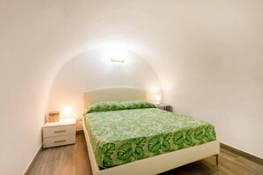 Un dormitorio con cama, mesita de noche y lámpara fijada a la pared.