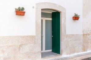 Un edificio con una puerta verde, una pared blanca y dos macetas en la pared.