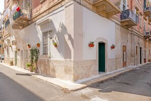 A narrow street with a building featuring a green door, potted plants, and a white facade.