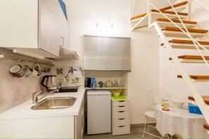 Una cocina compacta con un lavamanos, un refrigerador pequeño y una zona de comedor con una mesa y sillas.