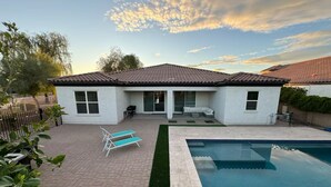 Una casa con piscina, un patio con sillones de descanso y una pequeña terraza.