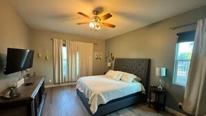 Un dormitorio con cama, ventilador de techo, televisor y ventana.