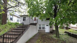 Ein zweistöckiges Haus mit Veranda, Treppe und Baum davor.