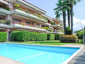 A multi-story hotel with a swimming pool, balconies with plants, and palm trees.