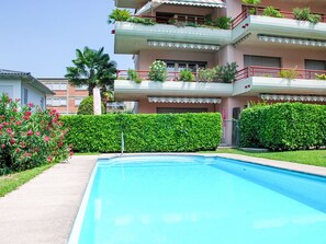 Un immeuble résidentiel doté d’une piscine, de balcons ornés de plantes et d’une haie bien entretenue.